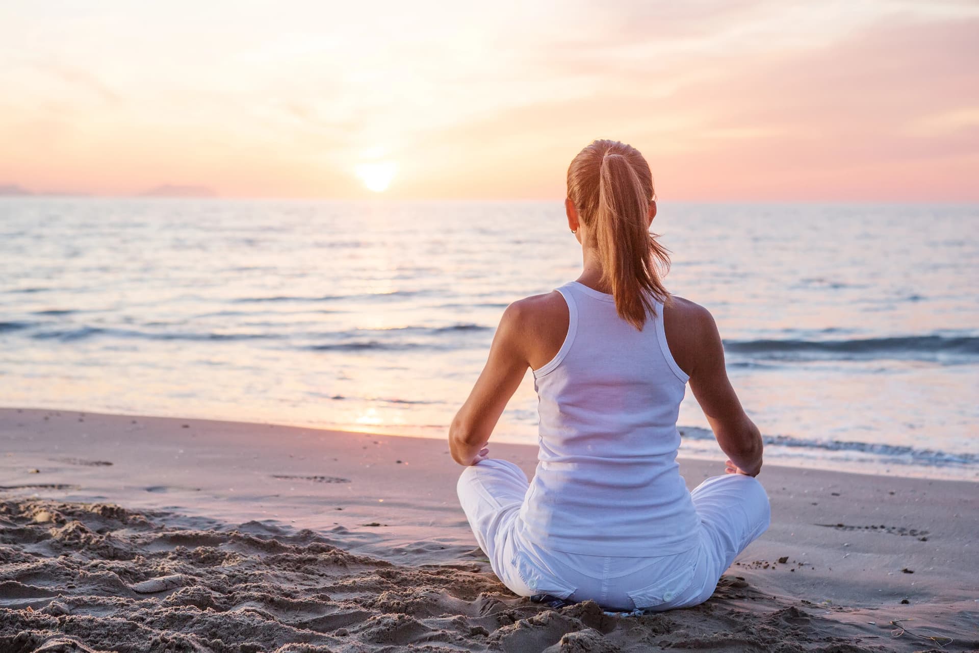 Ženska meditira na plaži ob sončnem zahodu